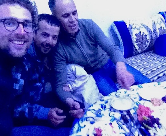 Dan, Mohamed and Ismain bunched together at the table, smiling at the camera. Ismain is half-wrestling with his tiny son, who his trying to hide from the camera behind Ismain's arm.